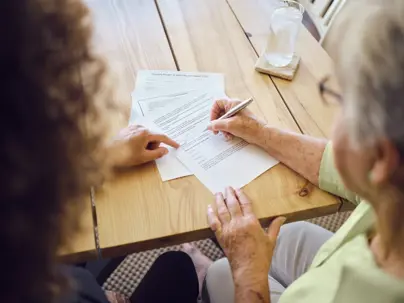 A senior aged woman signing documents with a financial adviser in her home.